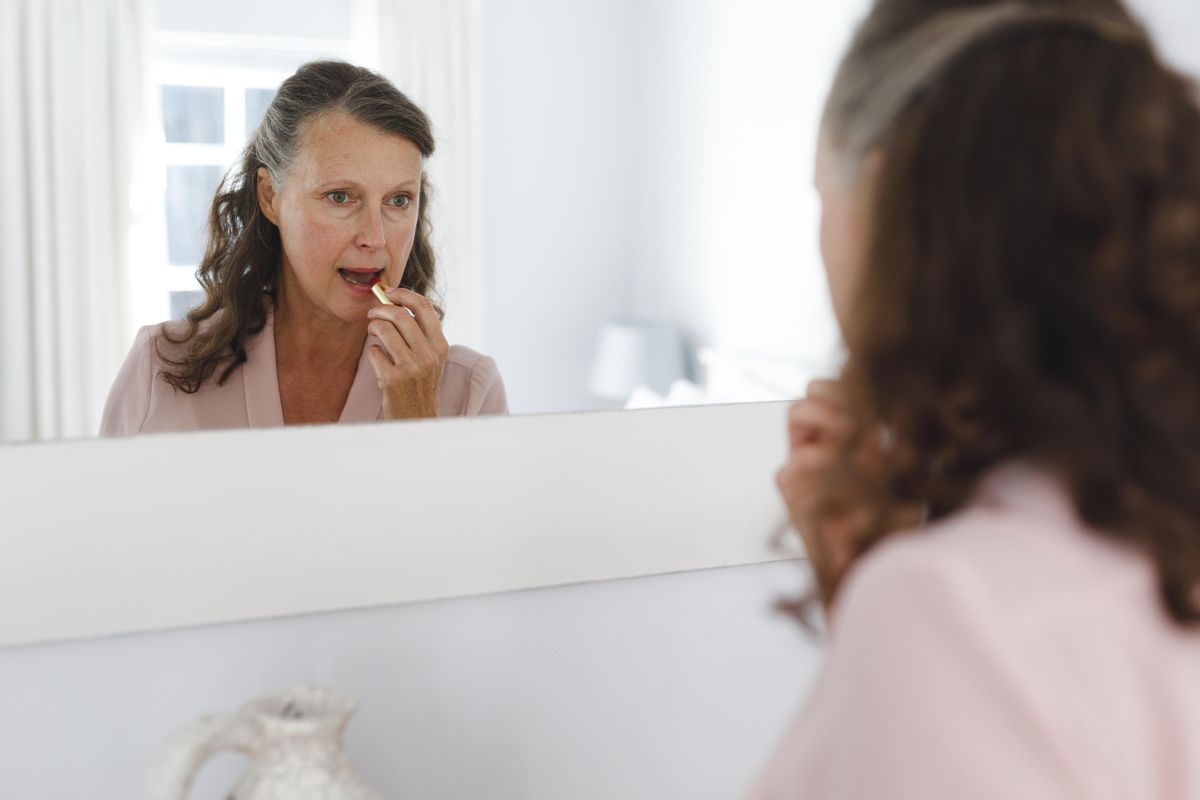 Una mujer frente al espejo pintándose los labios