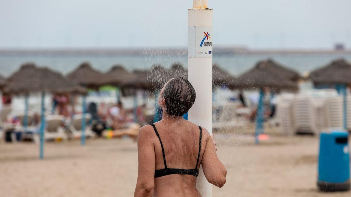 Una mujer se refresca en una de las duchas de una playa de València, ayer. | LOYOLA PÉREZ DE VILLEGAS