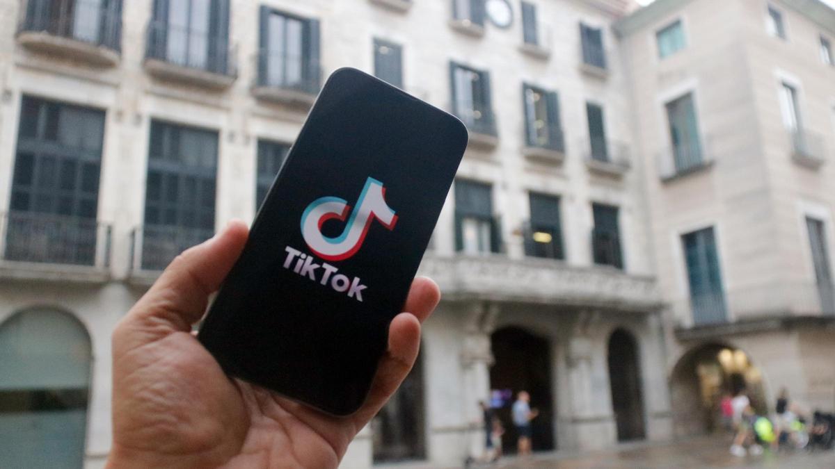 En primer terme, un mòbil amb el logotip d'una xarxa social; al fons, la façana de l'Ajuntament de Girona