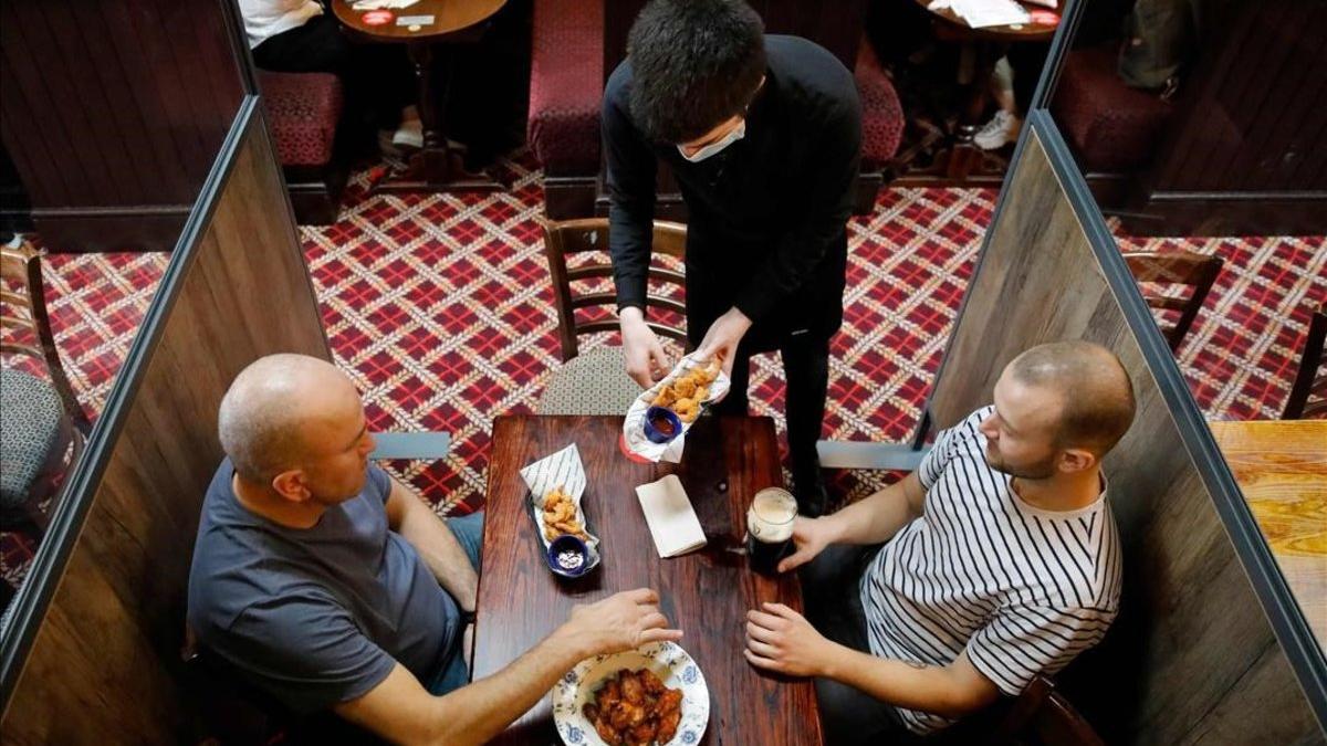 Un camarero protegido contra el covid sirve a los clientes en un pub de Londres.