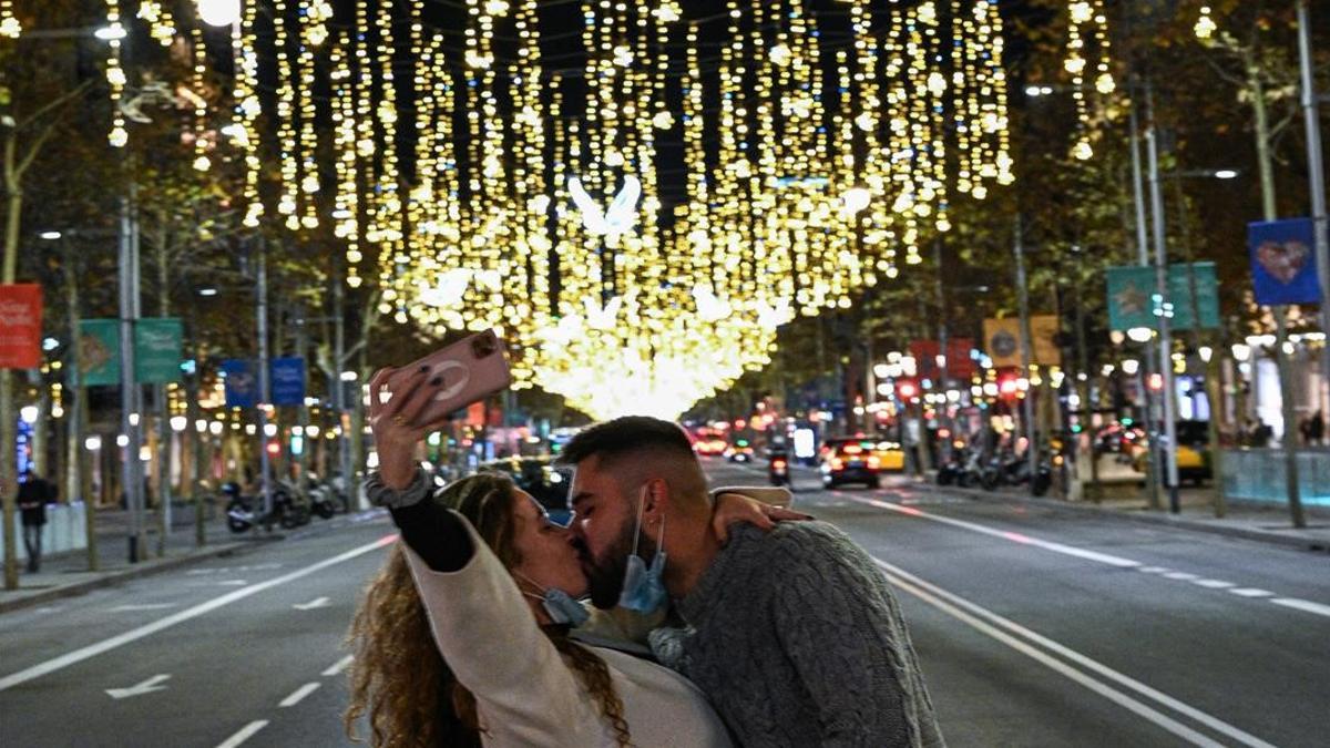 Una pareja se besa mientras se hace una selfie bajo la luz navideña en el paseo de Gràcia.