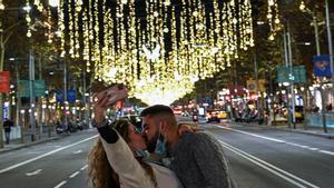 Una pareja se besa mientras se hace una selfie bajo la luz navideña en el paseo de Gràcia.