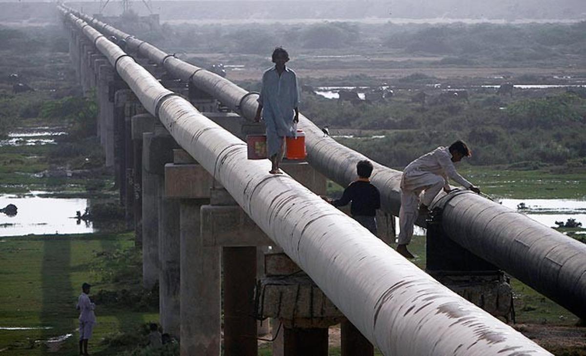 Un home amb dues galledes plenes d’aigua camina aquest dimecres per una canonada de Karachi, al Pakistan.