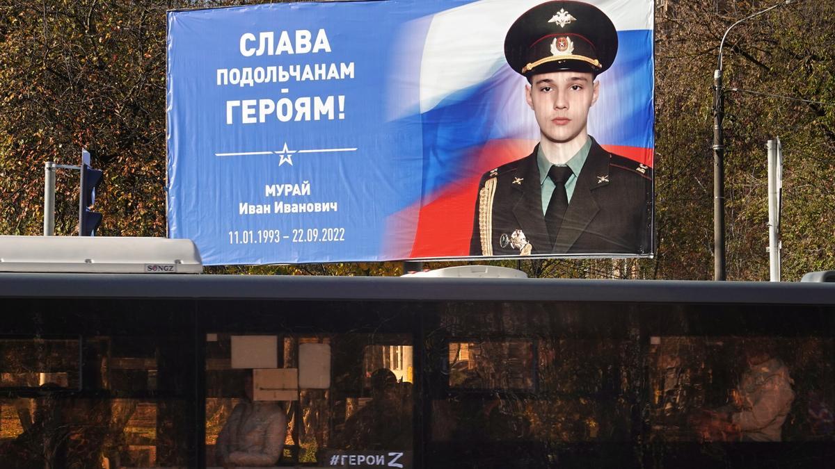 Un autobús con una pintada de la letra Z, en apoyo a la invasión de Ucrania, circula por un suburbio de Moscú junto a un poster con un retrato de un soldado ruso fallecido en la guerra.