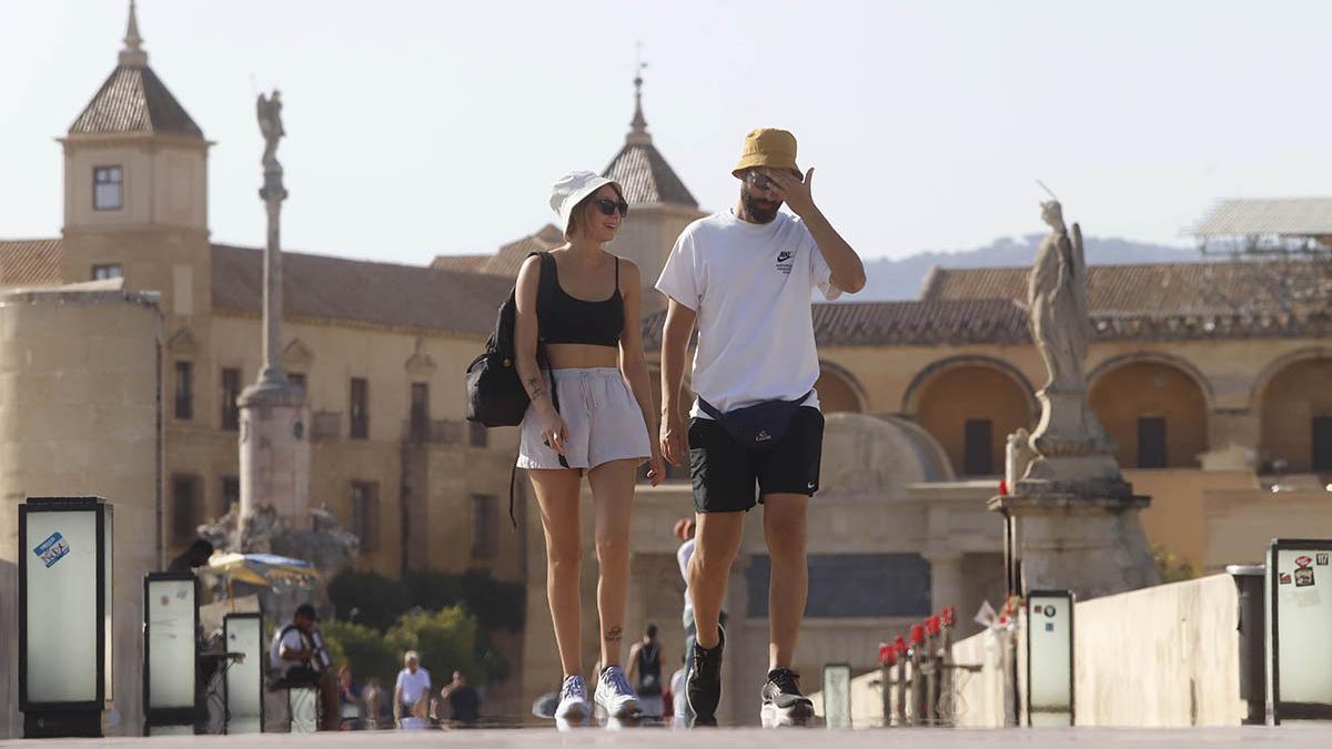 Dos viandantes se protegen del calor con un gorro en su paso por Córdoba.