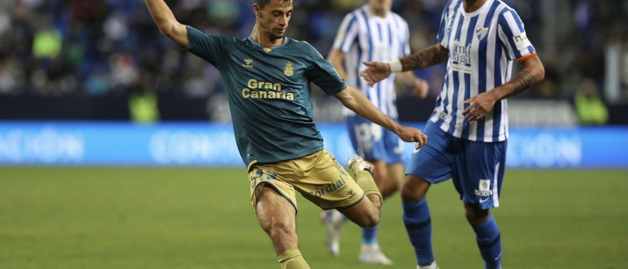 El centrocampista galo de Las Palmas Enzo Loiodice golpea el esférico ante el capitán del Málaga, Alberto Escassi.  | | LOF