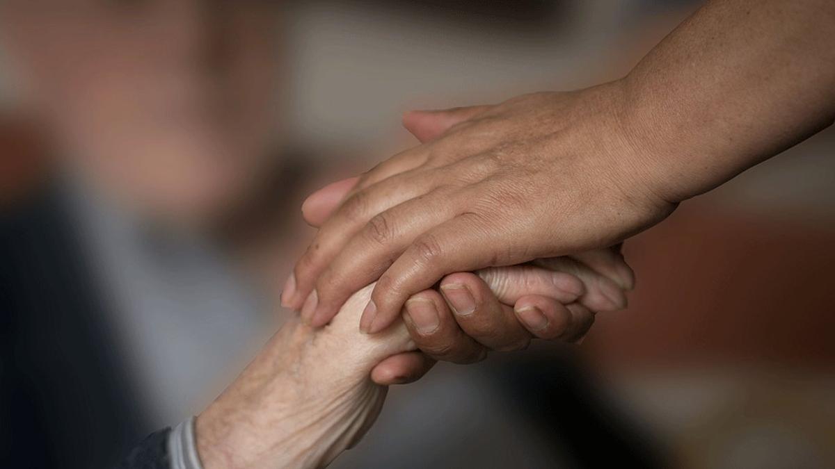 Una mujer coge la mano de una anciana, en una foto de archivo