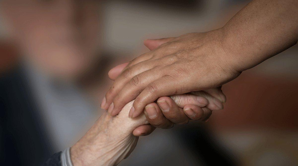 Una mujer coge la mano de una anciana, en una foto de archivo.