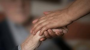 Una mujer coge la mano de una anciana, en una foto de archivo.