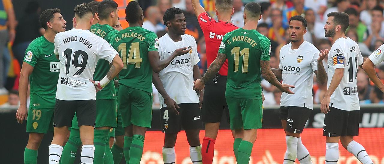 Los jugadores del Elche y del Valencia observan como el árbitro amonesta a Musah en la acción polémica del partido