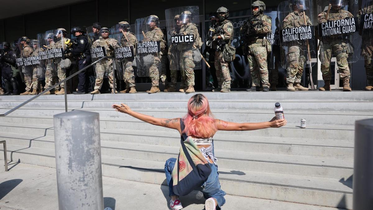 Una manifestante se arrodilla frente a miembros de la Guardia Nacional de California este lunes, frente al edificio federal Edward R. Roybal en Los Ángeles,