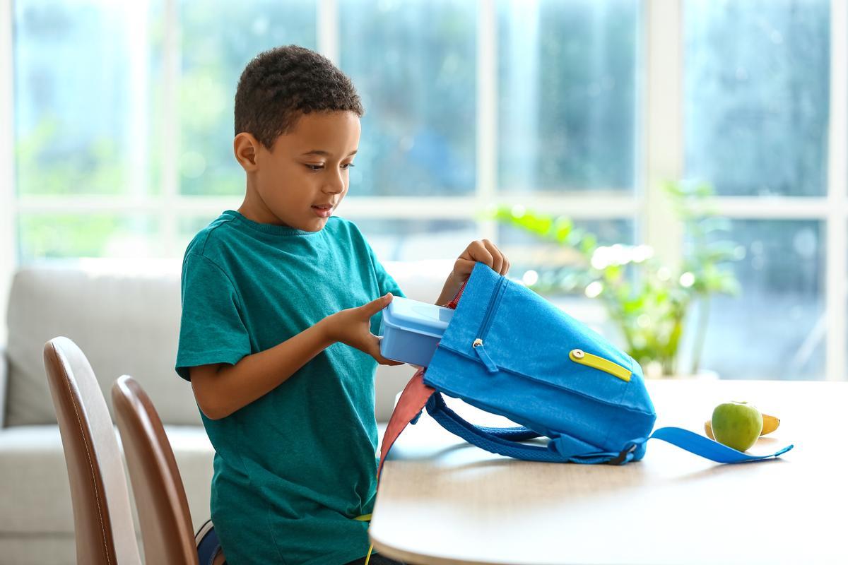 Un niño guarda el tupper con su almuerzo en su mochila.