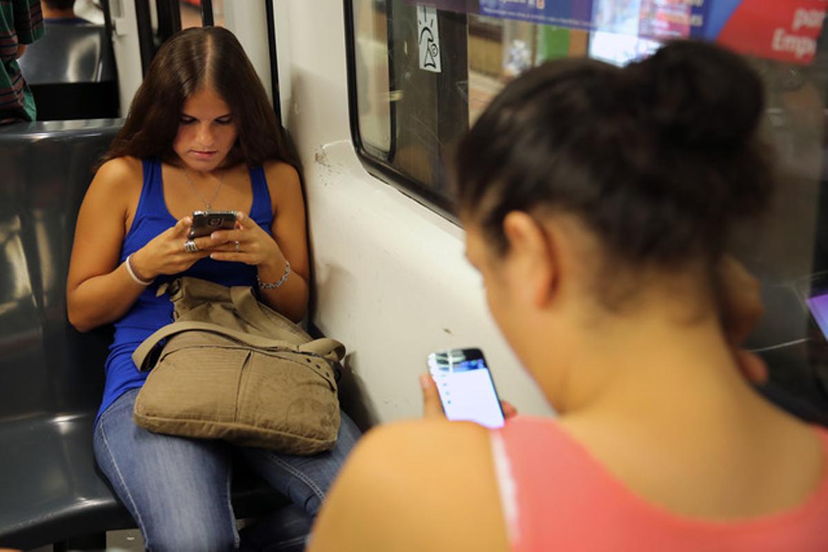 Dos chicas consultan en el metro sus respectivos móviles.