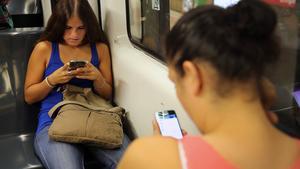 Dos chicas consultan en el metro sus respectivos móviles.