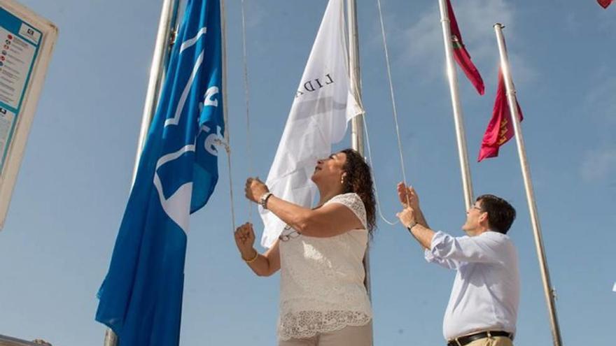 Los ediles Gómez (i.) y Aznar izan las banderas en Cala Cortina.