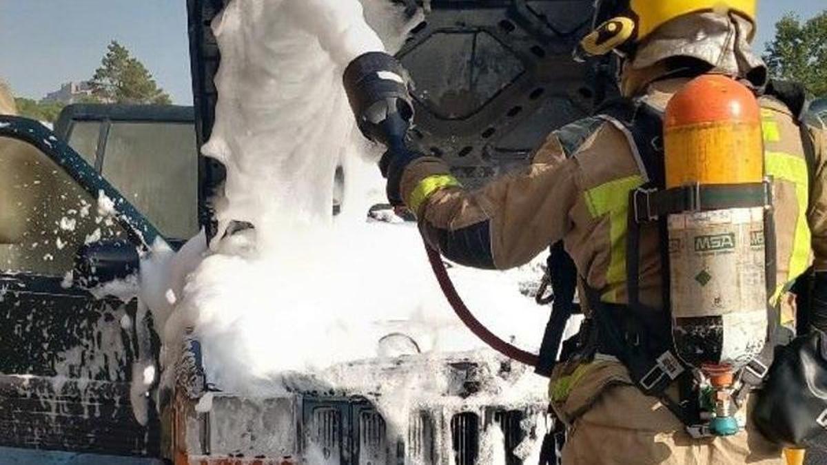 Un bombers ruixant amb escuma el cotxe que s'encenia