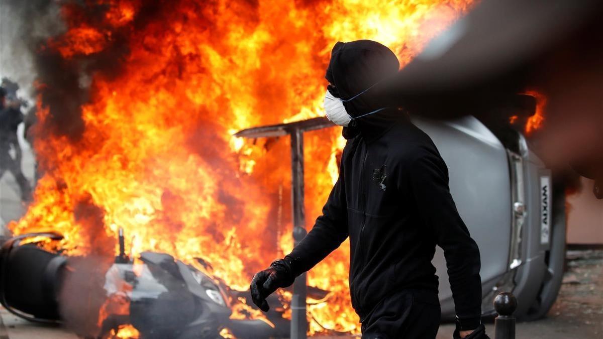 Un manifestante pasa junto a un coche en llamas, durante los disturbios del Primero de Mayo en París