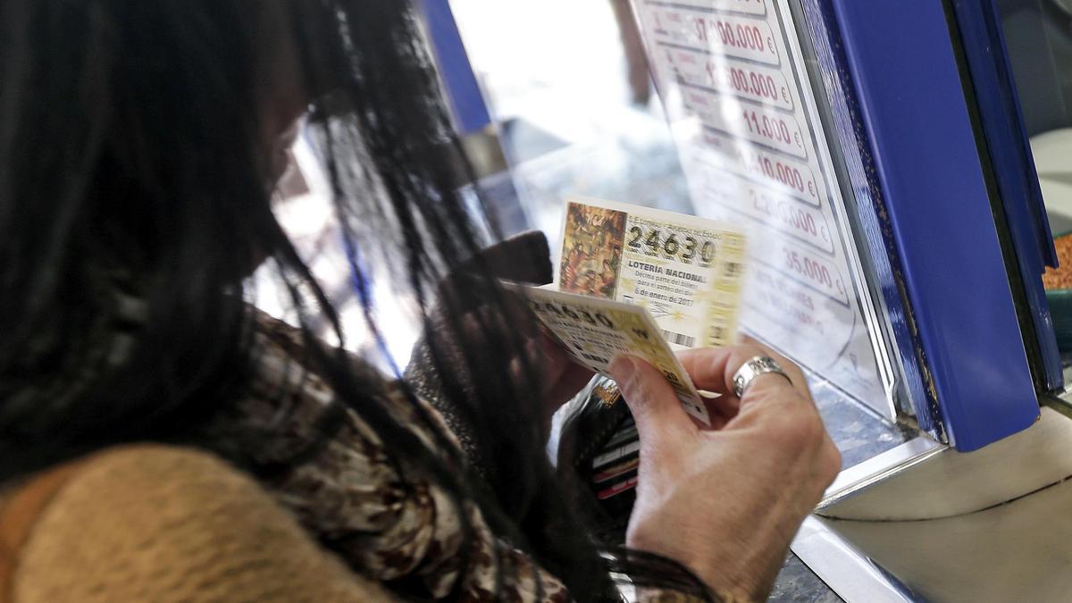 Una mujer sostiene dos décimos de Lotería de Navidad 2023.