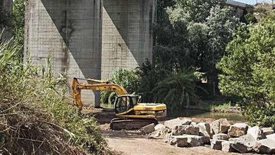 Una màquina treballant al punt del riu on es construïrà la passera, sota el viaducte