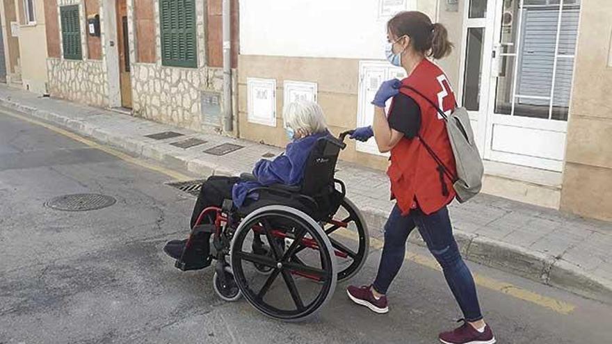 Una voluntaria de Cruz Roja pasea a una anciana en silla de ruedas durante el estado de alarma.