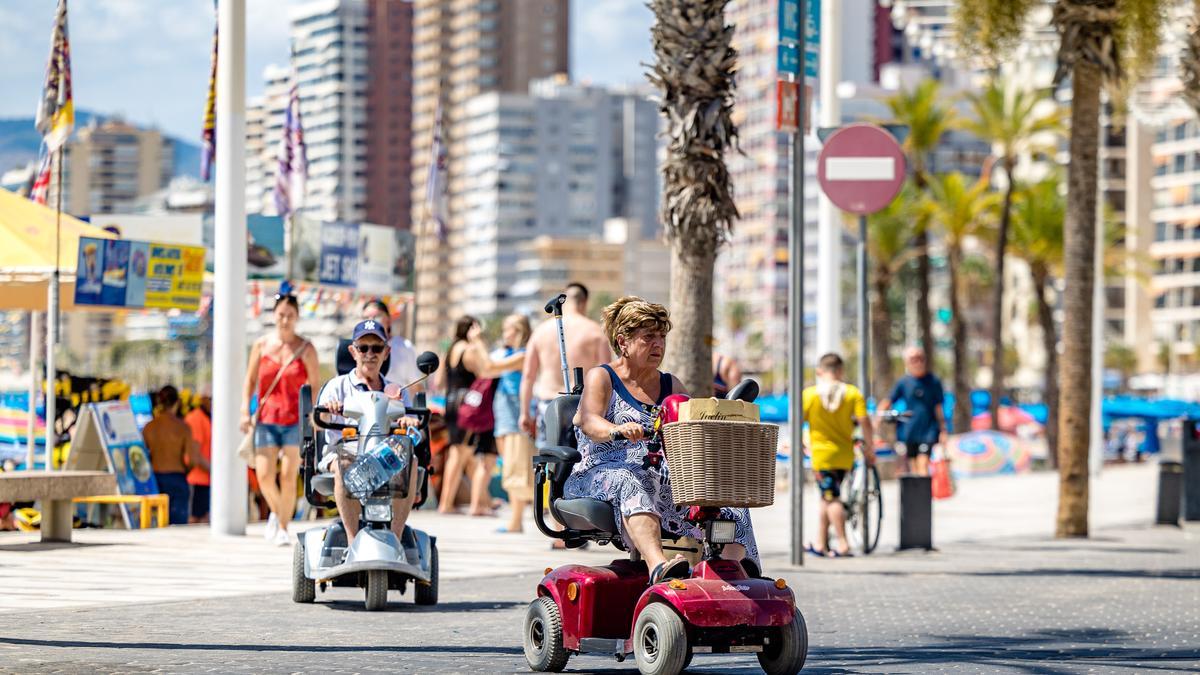 Dos personas de edad circulan con su &quot;scooter&quot; eléctrica por el paseo de Levante de Benidorm, este jueves.