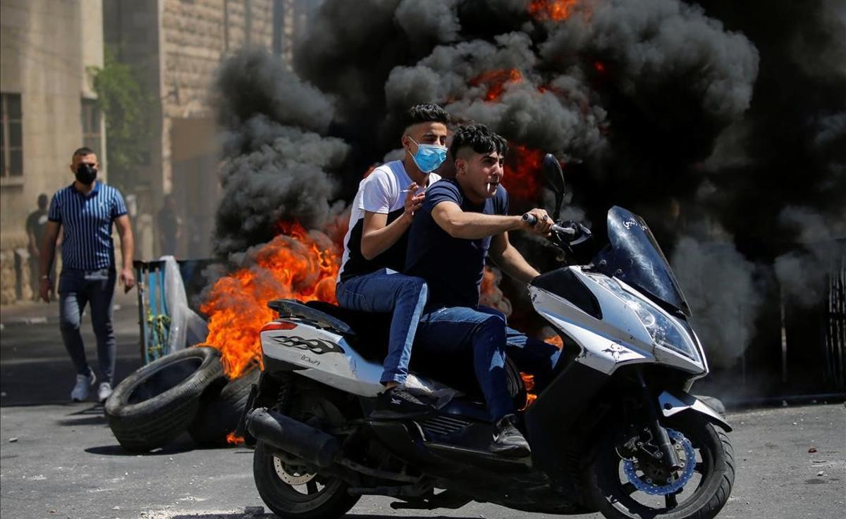 Manifestantes palestinos en moto, frente a unos neumáticos quemados, durante las protestas en Hebrón.