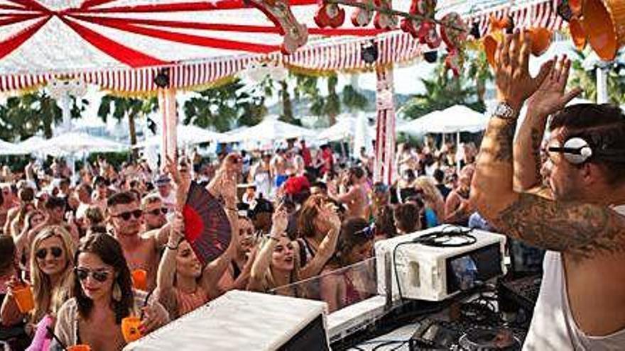 Una multitud de personas baila al son de la música de un dj en un &#039;beach club&#039; de la isla.