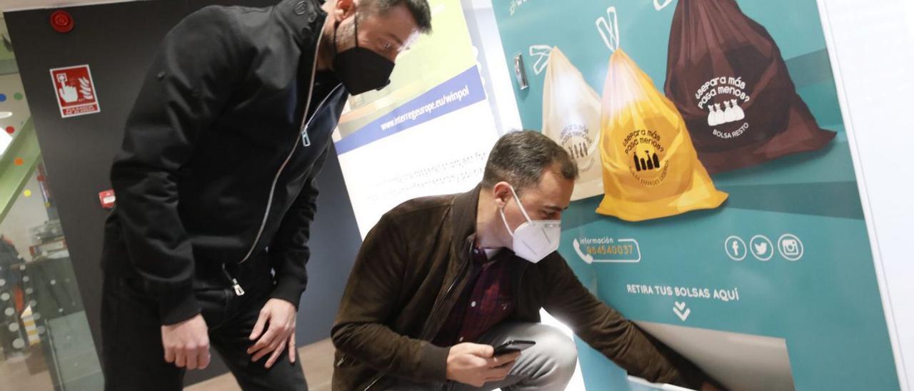 Olmo Ron recoge de la máquina expendedora una de las nuevas bolsas de la campaña ante Alfonso Baragaño, ayer, en la sede de las oficinas de Emulsa, en Roces. | Ángel González