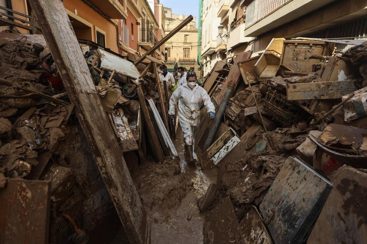 Una mujer camina por un pasillo de escombros y basura en Paiporta