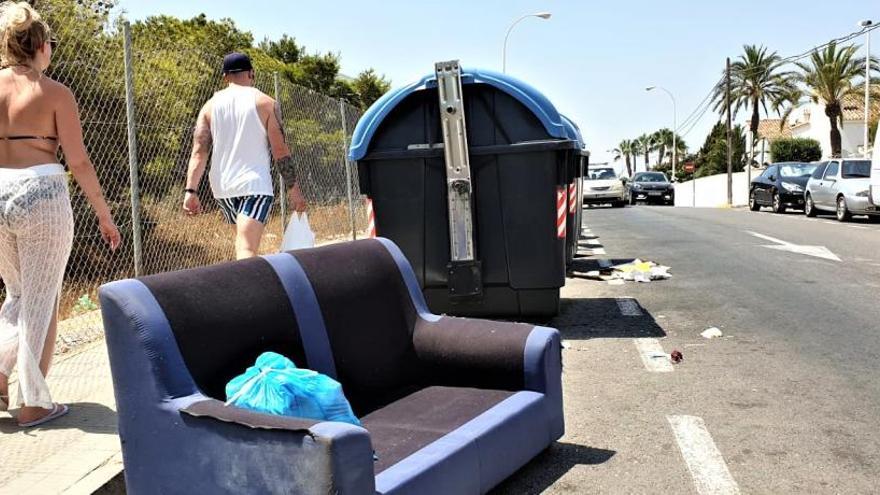 Veraneantes paseando ayer junto a un sofá abandonado en una avenida de Gran Alacant.