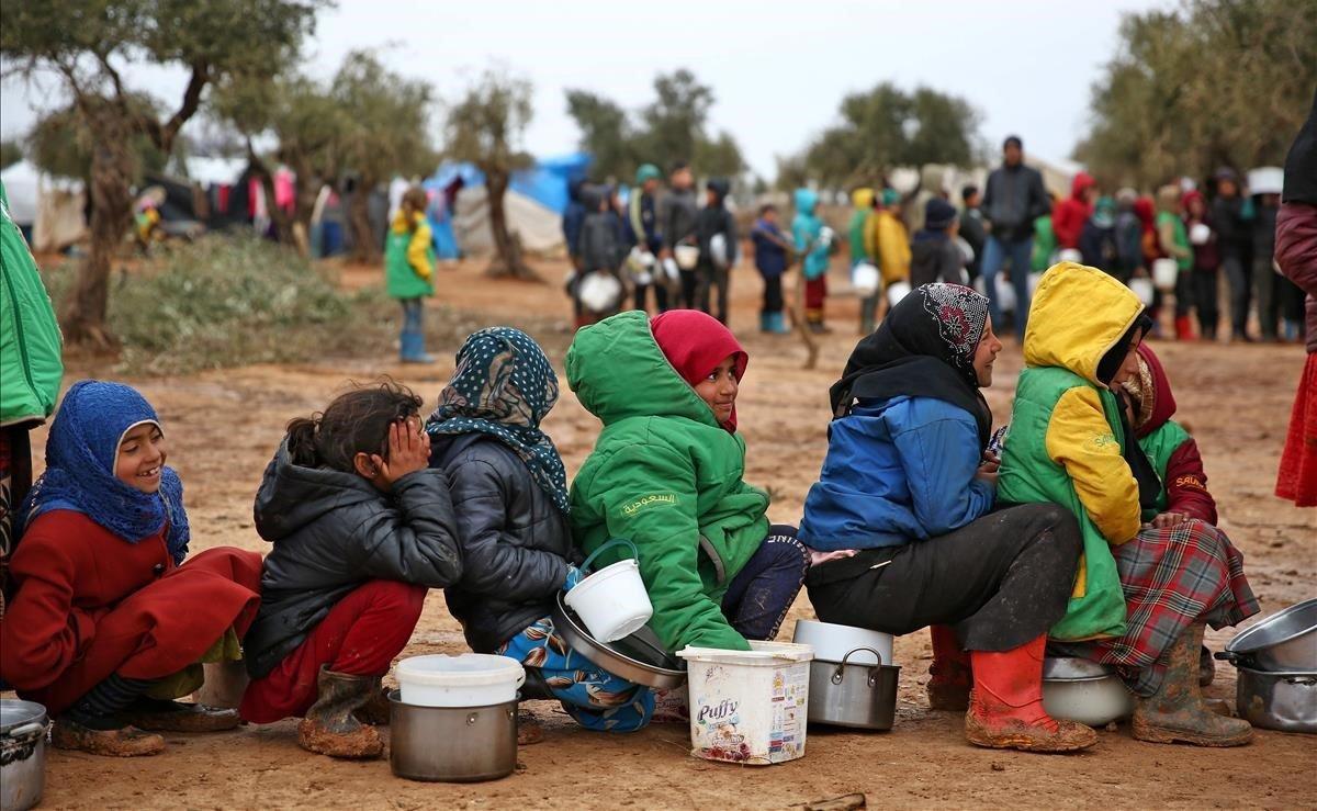 Niños sirios hacen cola para recibir alimentos distribuidos por trabajadores humanitarios, en un campamento improvisado para personas desplazadas cerca de la aldea de Yazi Bagh.