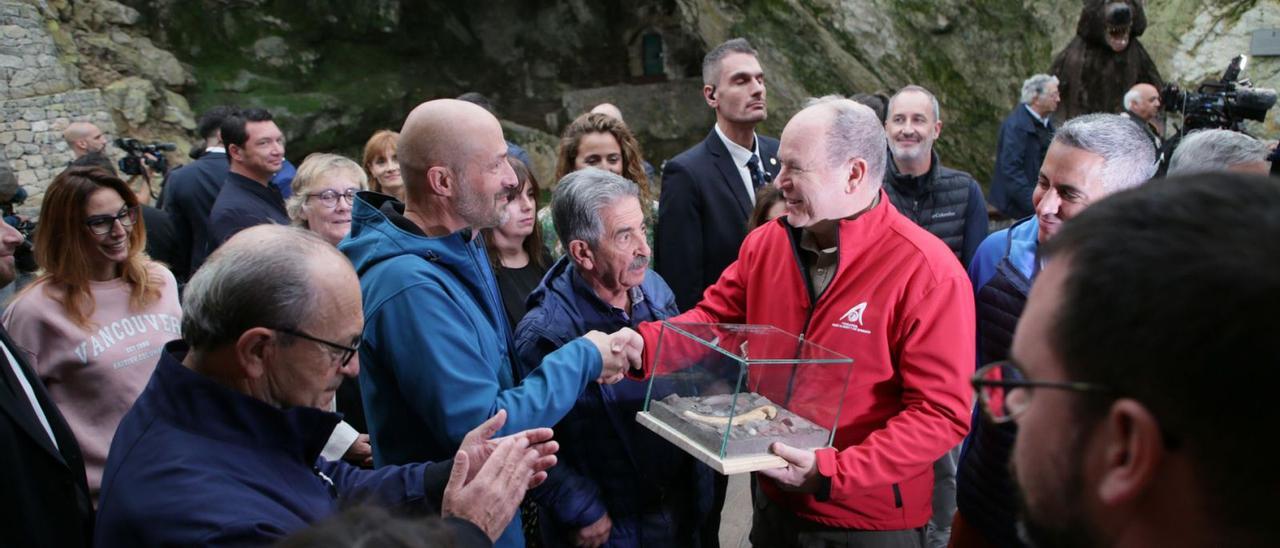 Alberto II de Mónaco, con chaqueta roja, recibe un obsequio durante su visita al futuro Centro de Arte Rupestre de Puente Viesgo. | Europa Press