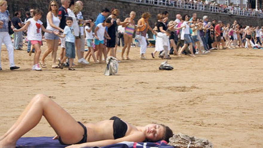 Una joven toma el sol, en primer término, mientras centenares de personas bailan la danza prima al fondo