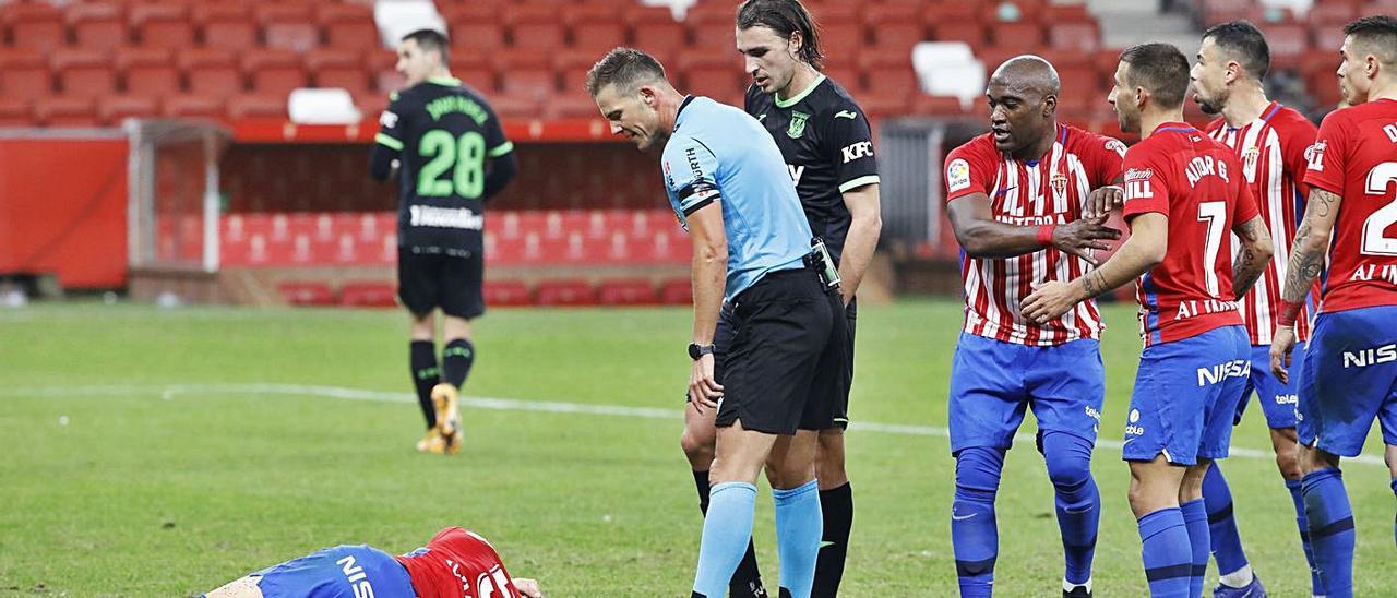 Pulido Santana se dirige a Borja López –en el suelo–, tras recibir el golpe de Cuéllar en la acción que el VAR acabó decretando penalti a favor del Sporting en el partido ante el Leganés. | Ángel González