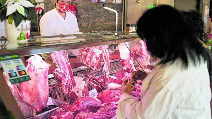 Una carnicera atiende a una cliente frente a un expositor lleno de productos.