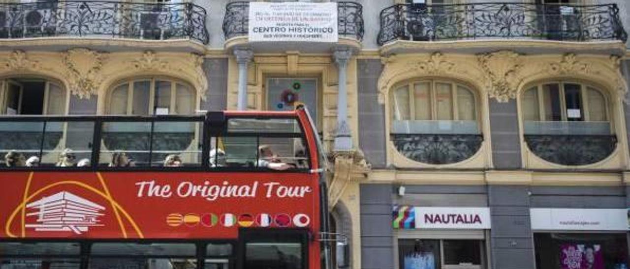 Un autobús turístico frente a un edificio en València con un cartel donde se rechazan los alquileres ilegales en el casco antiguo.