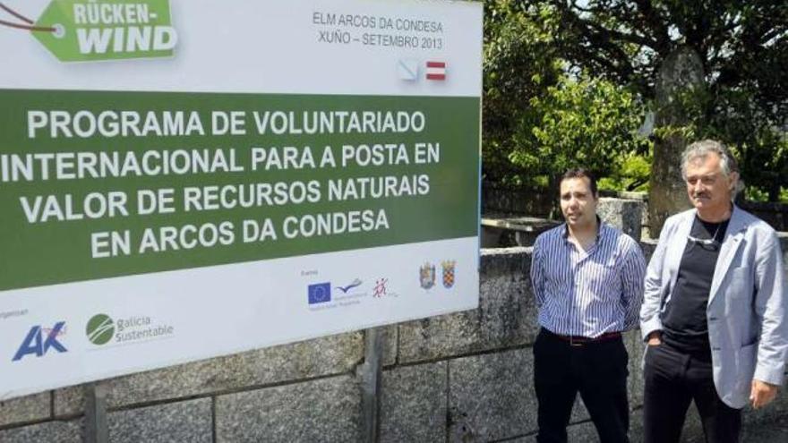 El alcalde pedáneo y el regidor, ante el cartel que anuncia el proyecto de voluntariado.  // Noé Parga