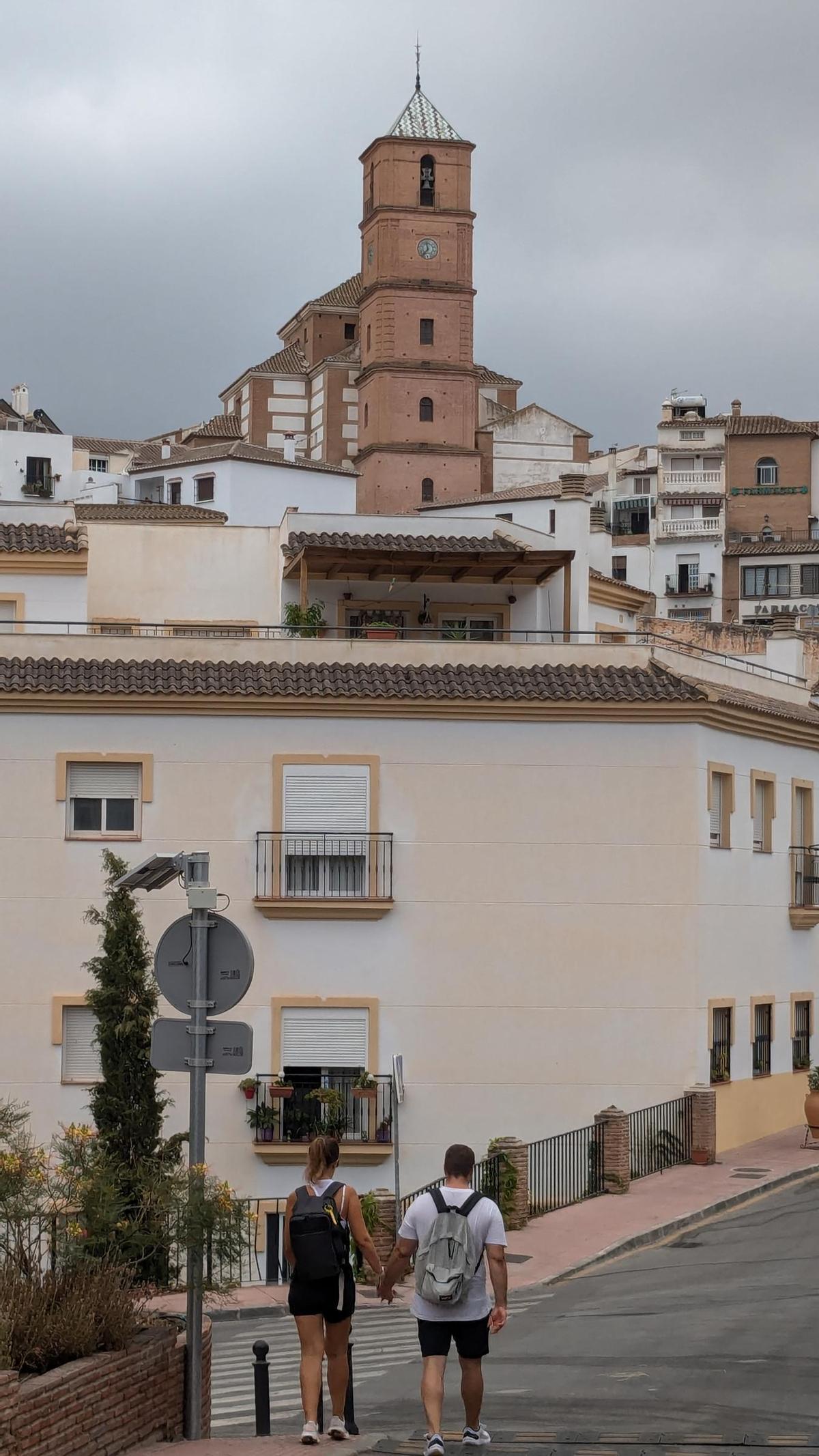 Dos turistas pasean por Casabermeja. De fondo, la iglesia de Nuestra Señora del Socorro