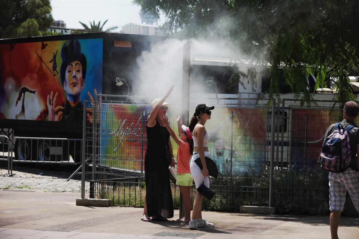  Unos turistas intentan refrescarse en unos vaporizadores de agua fresca instalados en los refugios climáticos del Passeig Joan de Borbó, en la Barceloneta.
