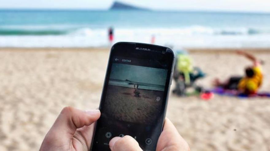 Un turista fotografía con su móvil la playa de Levante de Benidorm para subirlo a la red social Instagram.