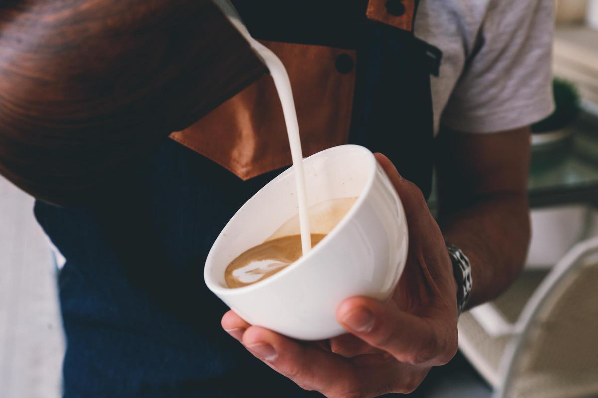 Un barista virte leche en una taza de café de especialidad.