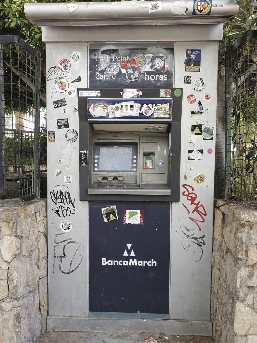 Un cajero automático situado en una de las calles de la playa lleno de grafitis y pegatinas.