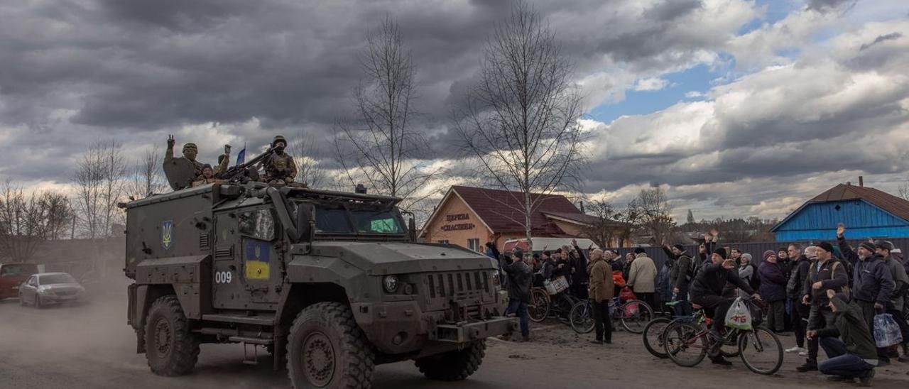 Soldados ucranianos saludan desde un vehículo militar a un grupo de personas que hacen cola para recibir ayuda humanitaria, en el pueblo de Trostyanets, en la región de Sumi.