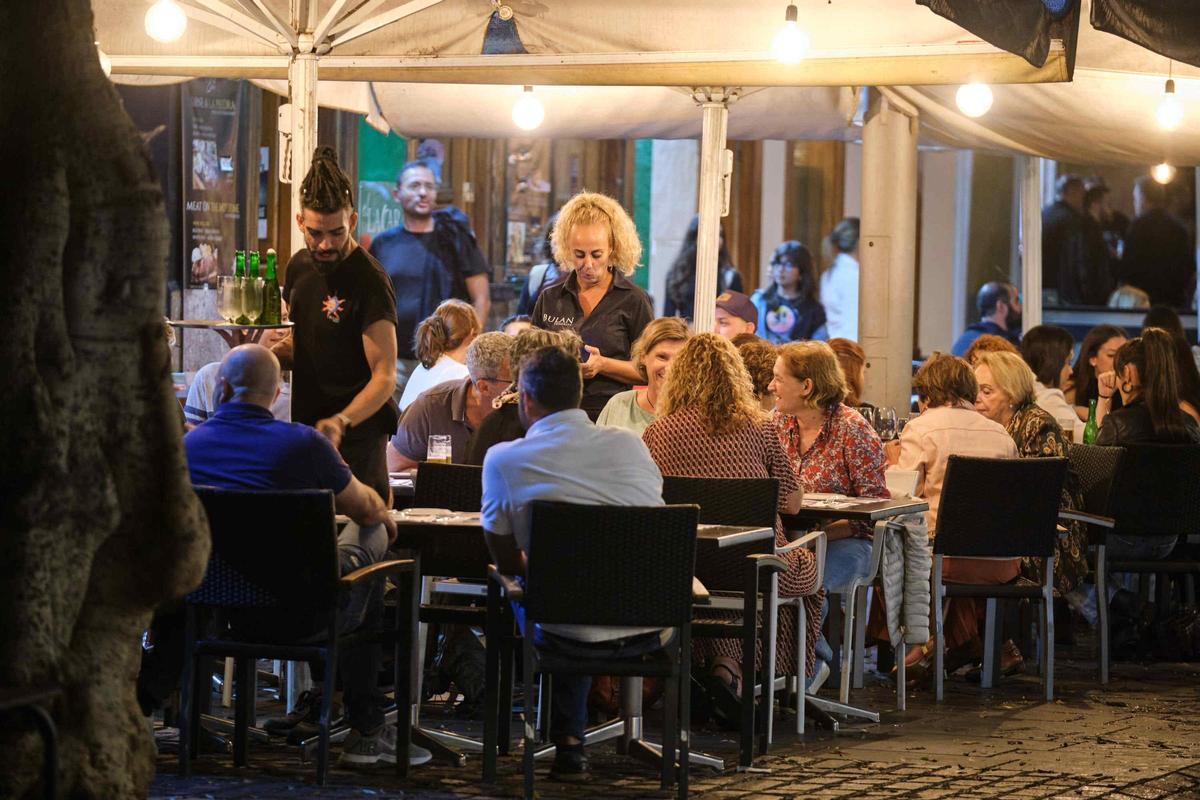 Varios camareros atienden las mesas de una terraza.