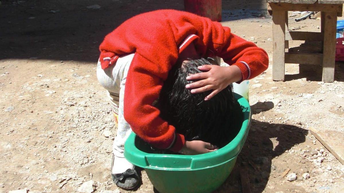 Una joven de Cajamarca se lava la cabeza con agua de una tina.