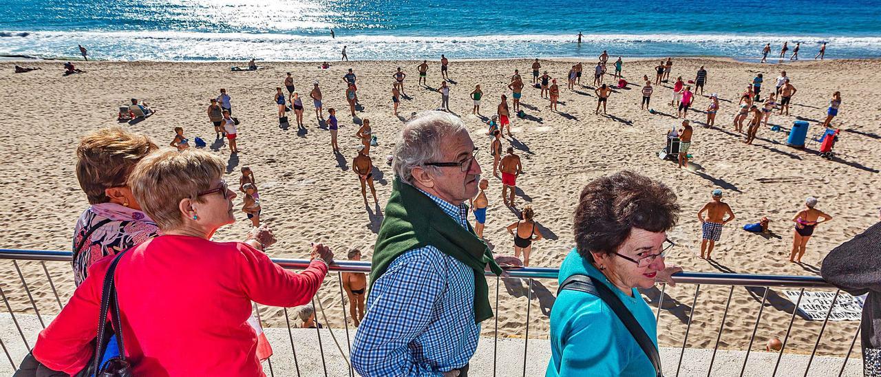 Un grupo de jubilados del Imserso pasea por el paseo de playa de Levante de Benidorm mientras otros hacen gimnasia a primera hora en una imagen de 2019. | DAVID REVENGA