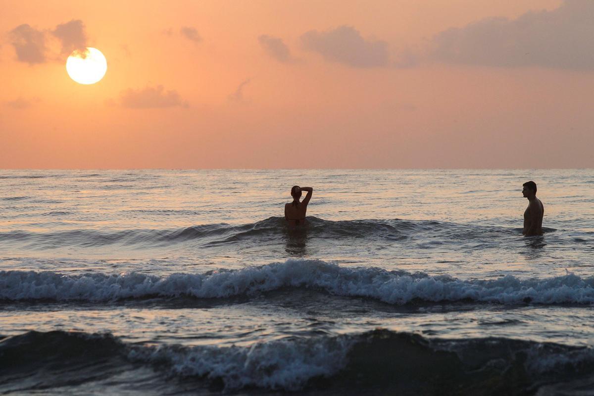 Dos turistas se bañan al amanecer en la playa de la Malvarrosa (Valencia).