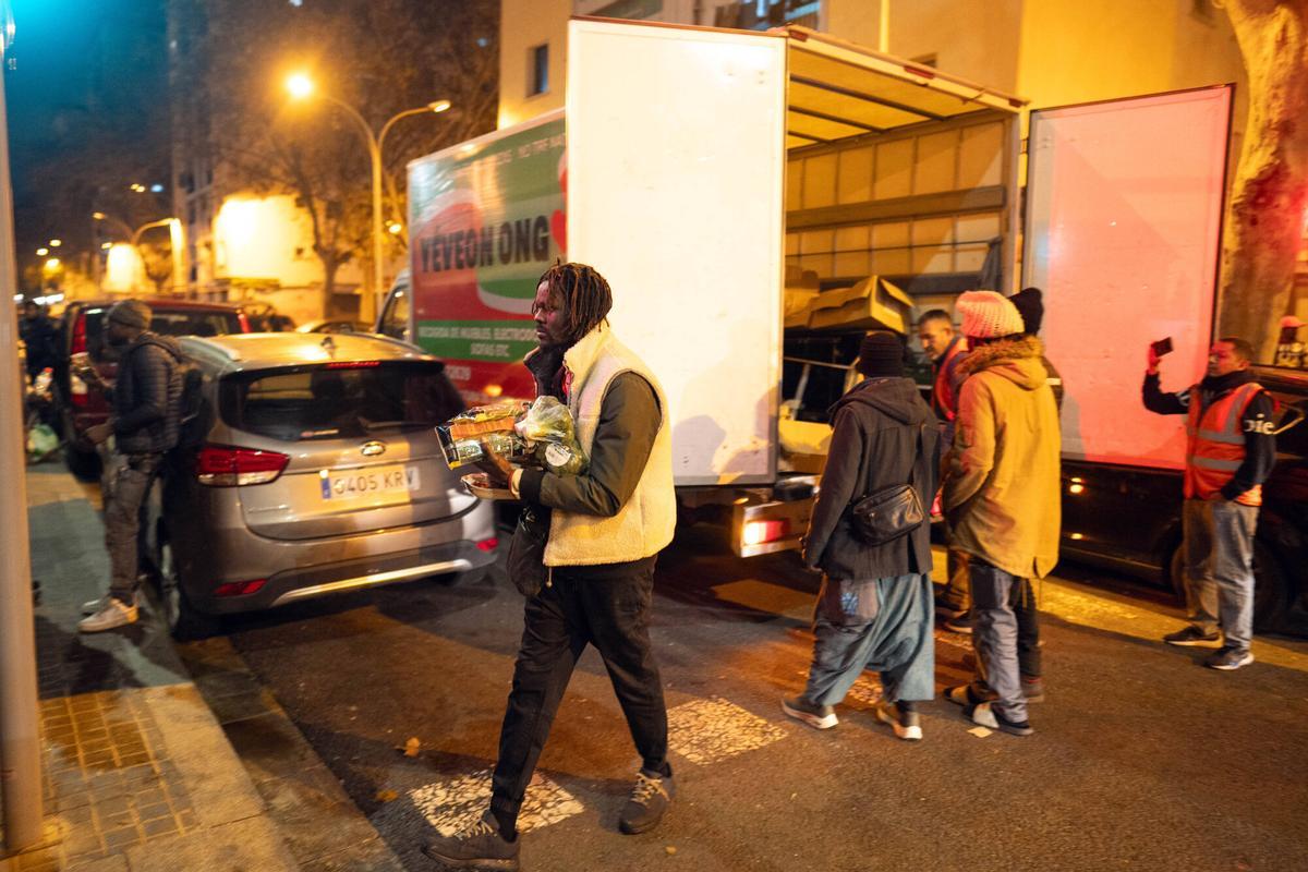 Voluntarios de distintas entidades privadas reparten comida para la cena de Nochebuena bajo la autopista C-31, donde aún duermen decenas de personas desalojadas del antiguo instituto B9