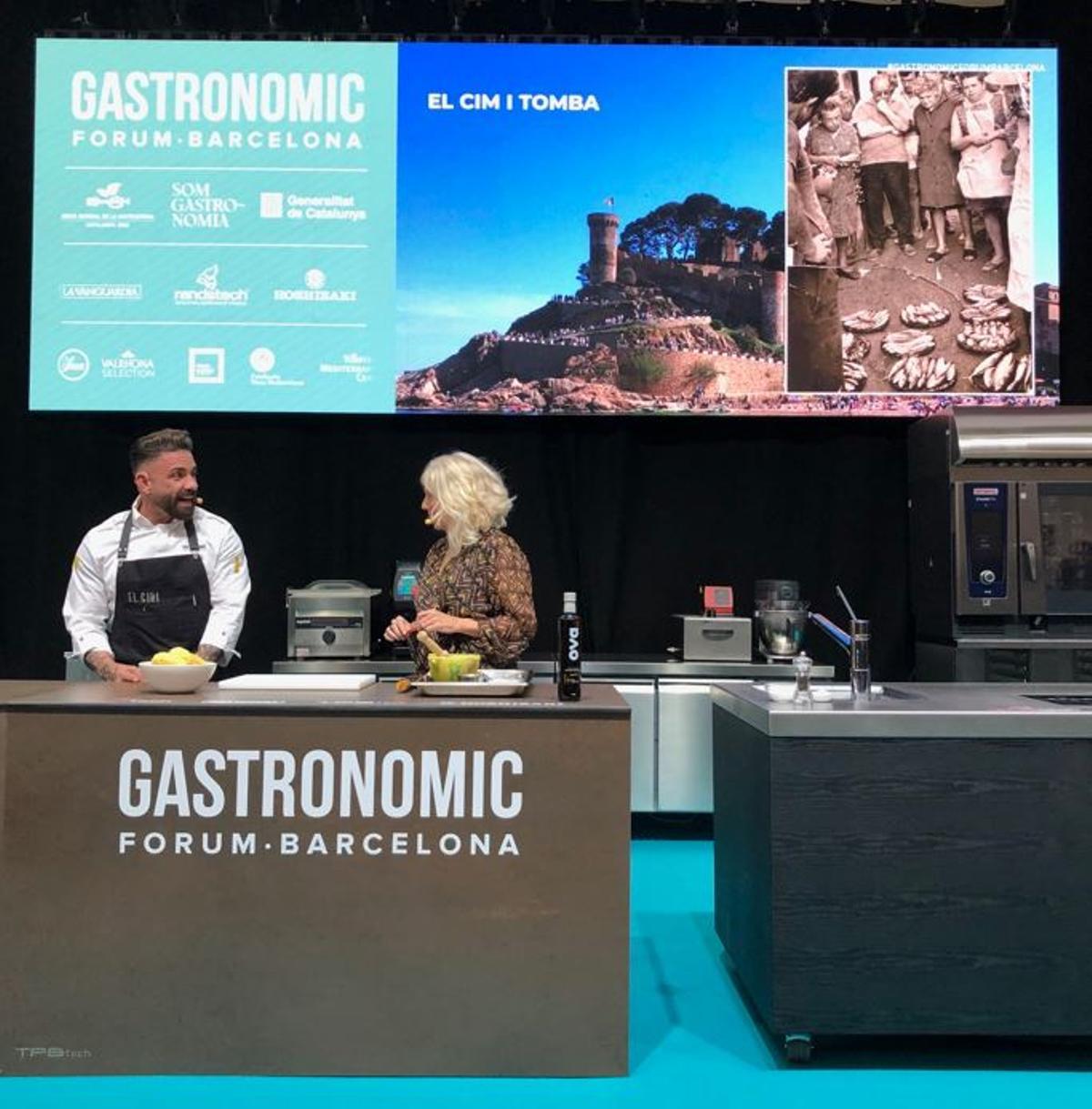 El xef Marc Ribas i la periodista Carme Gasull davant d’una imatge projectada de Tossa de Mar, en la sessió dedicada al cim i tomba.