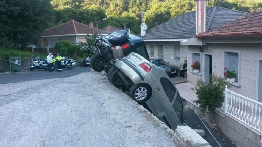 Los dos automóviles, colgando casi a la par del desnivel de la carretera, a pocos metros de casas. // FdV